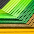 Close-up abstract image of colorful layered paper sheets in green, yellow, and gray creating geometric patterns.